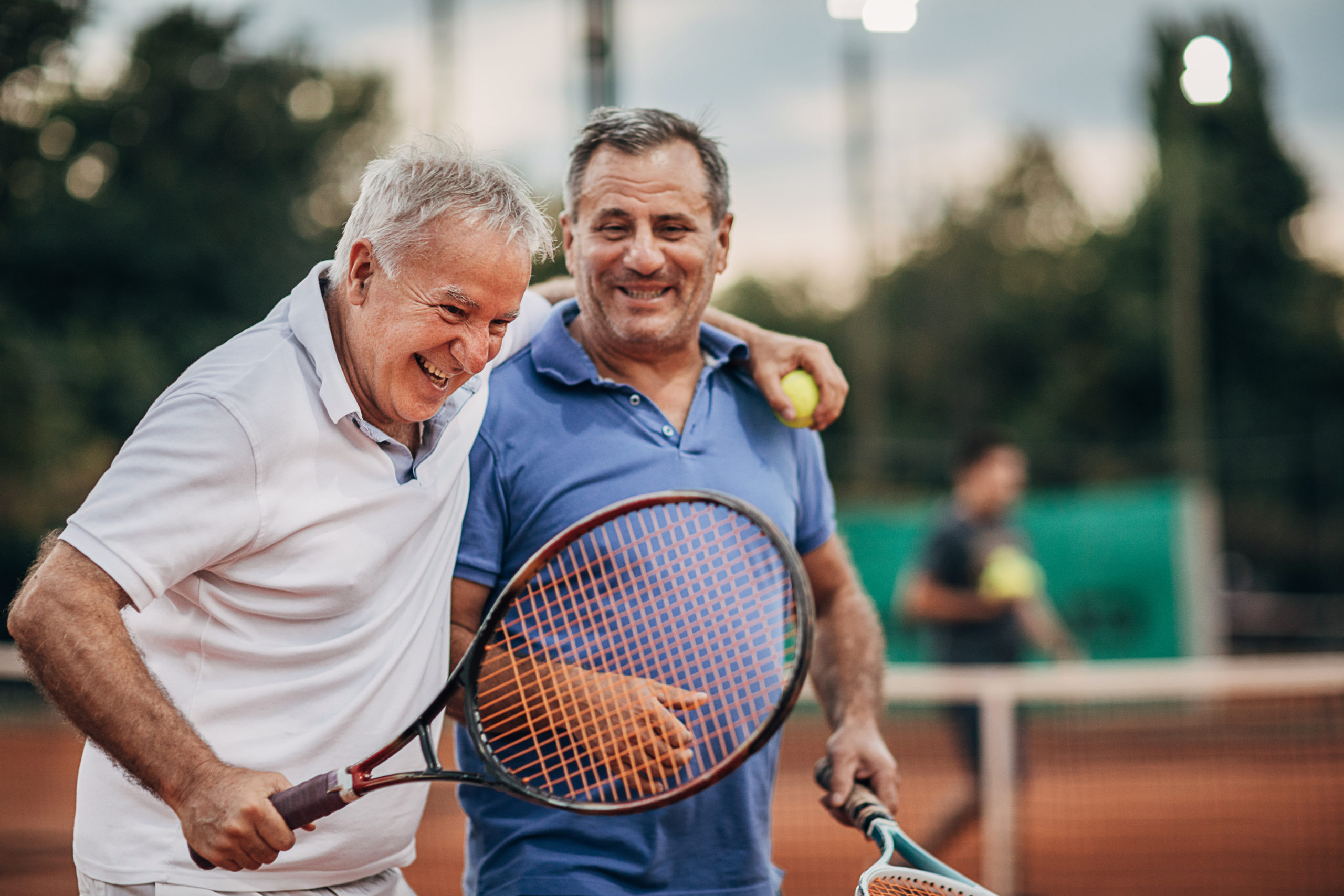 Two cheerful senior men talking while walking on the outdoor tennis court